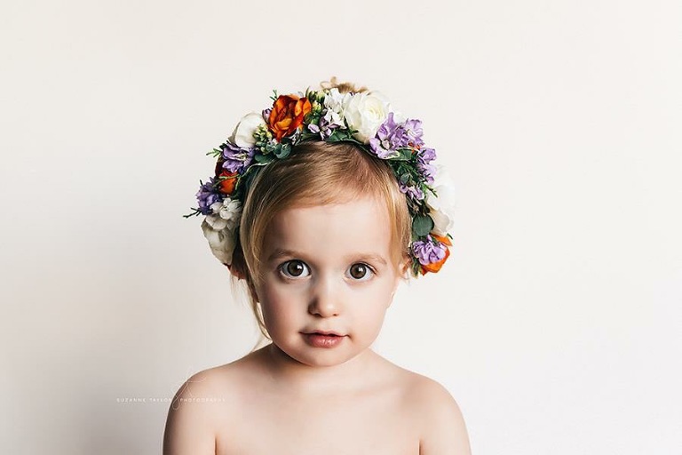 A toddler girl wearing a floral crown facing the camera.