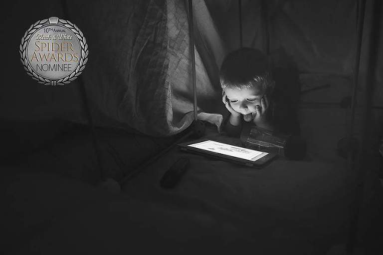 Young boy under a fort watches a show on the iPad with his tongue sticking out.